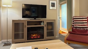 Una sala de estar con televisor de pantalla plana, chimenea, un sillón rojo y una lámpara de pie.