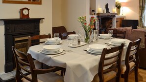 Een eetkamer met een tafel gedekt voor vier personen, een open haard en een klok aan de muur.