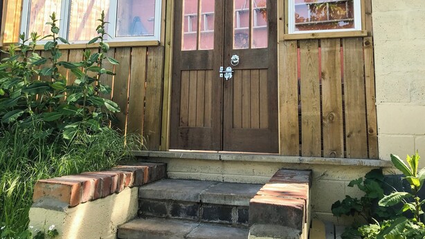 Een houten voordeur met een klein portaaltje en een trap ernaartoe.