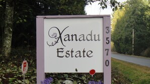 Señal para Nanadu Estate con los números 3, 5, 7, 0, rodeada de follaje y flores.