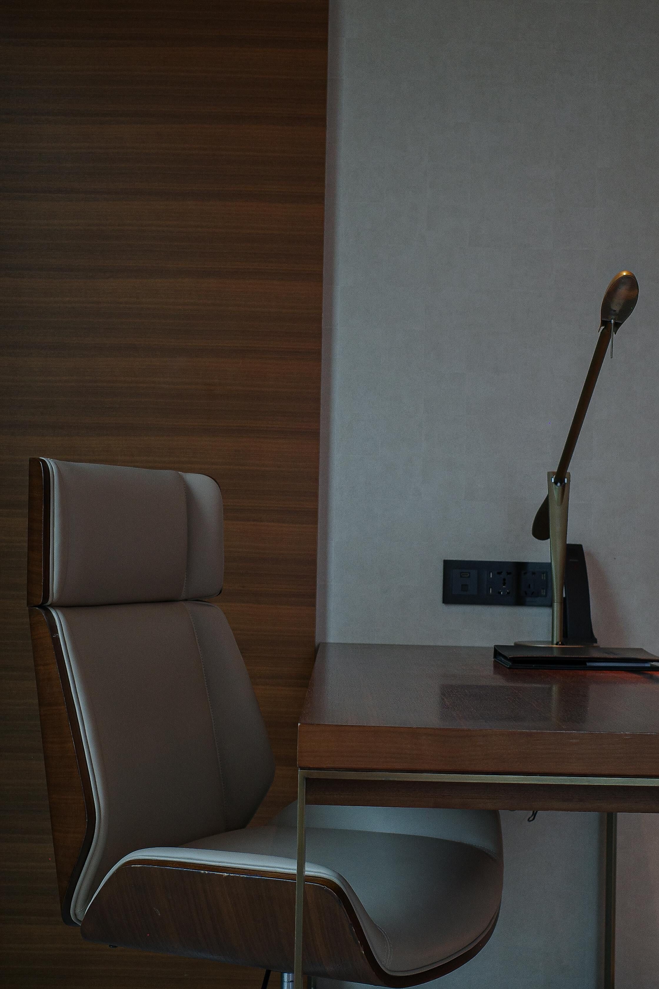 A modern office chair with a sleek design, positioned next to a wooden desk with a metallic lamp.