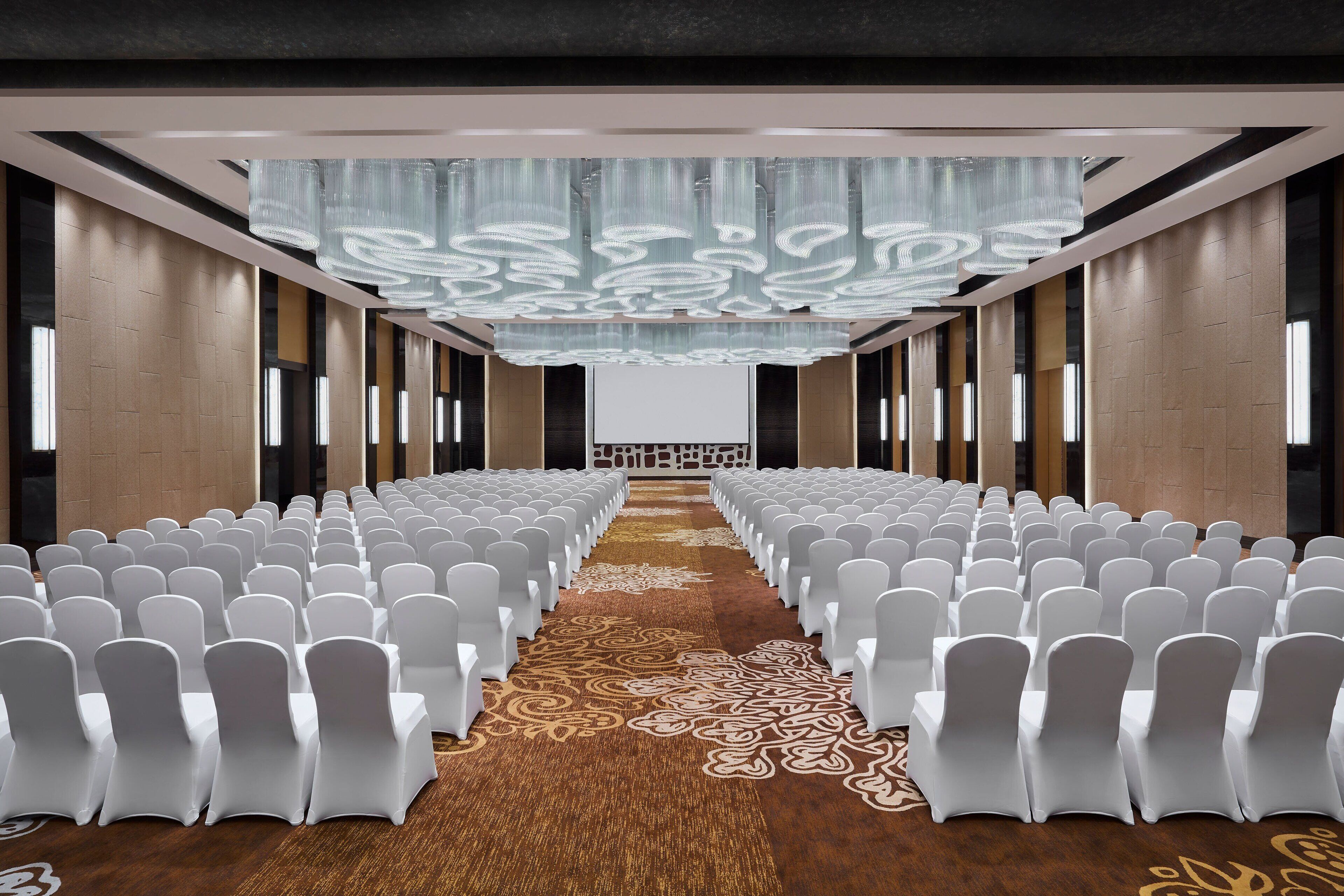 A conference room with rows of white chairs, a patterned carpet, and a modern chandelier.