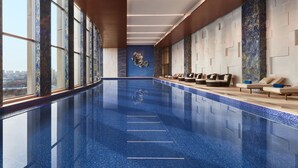 A long indoor swimming pool with clear blue tiles, a city view, and a row of lounge chairs along the side. - Sheraton Beijing Lize Hotel (Beijing)
