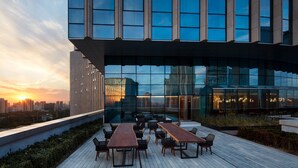 A rooftop terrace with a long wooden table and chairs, surrounded by glass walls offering city views. - Sheraton Beijing Lize Hotel (Beijing)
