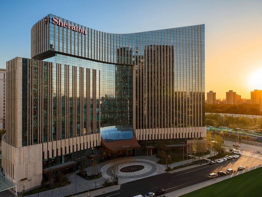 Un hotel moderno con fachada de vidrio curva, una entrada destacada y un área ajardinada con acceso circular.