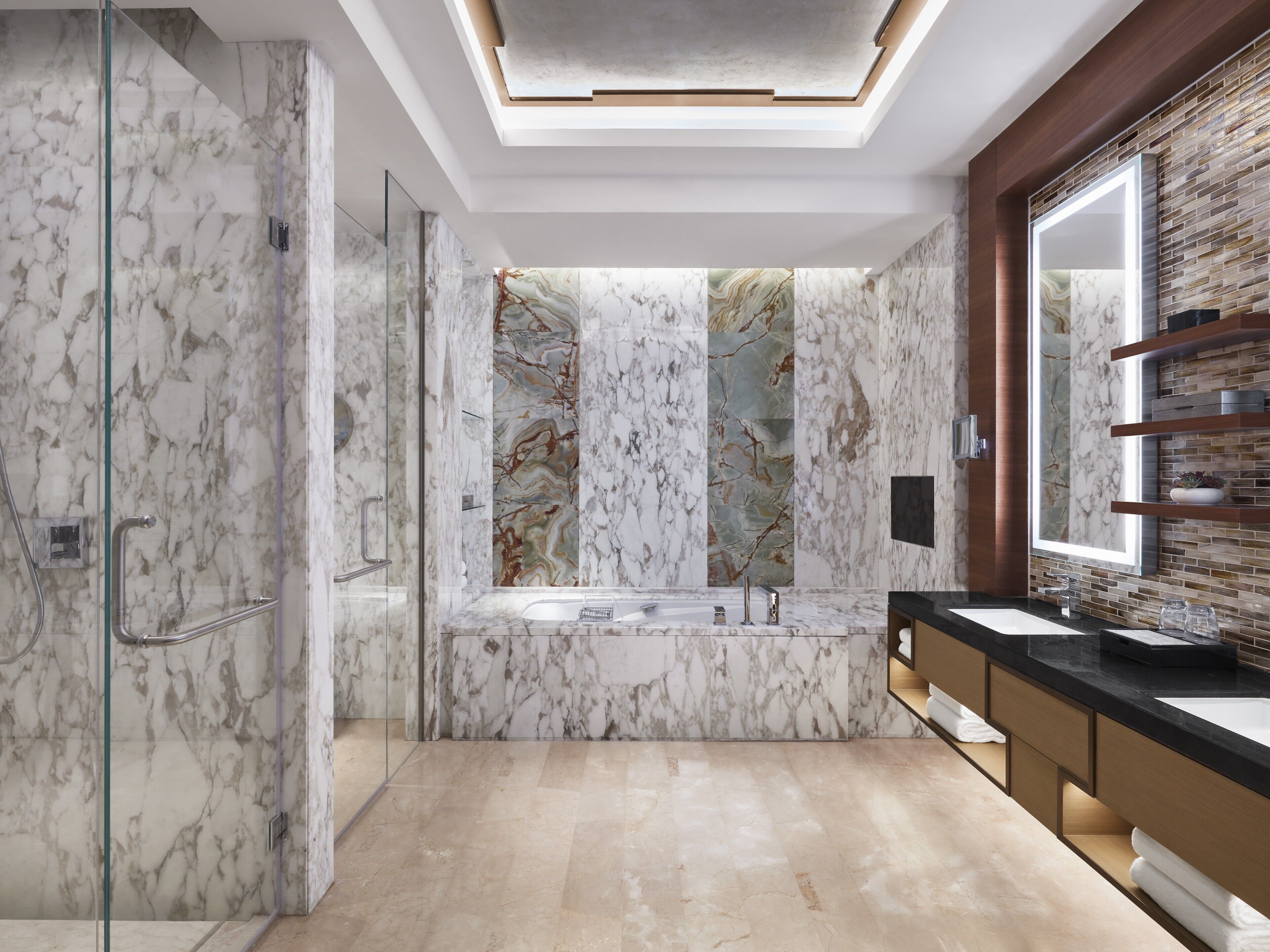 A modern bathroom with a glass-enclosed shower, a marble wall with a central column, and a large mirror above the sink.