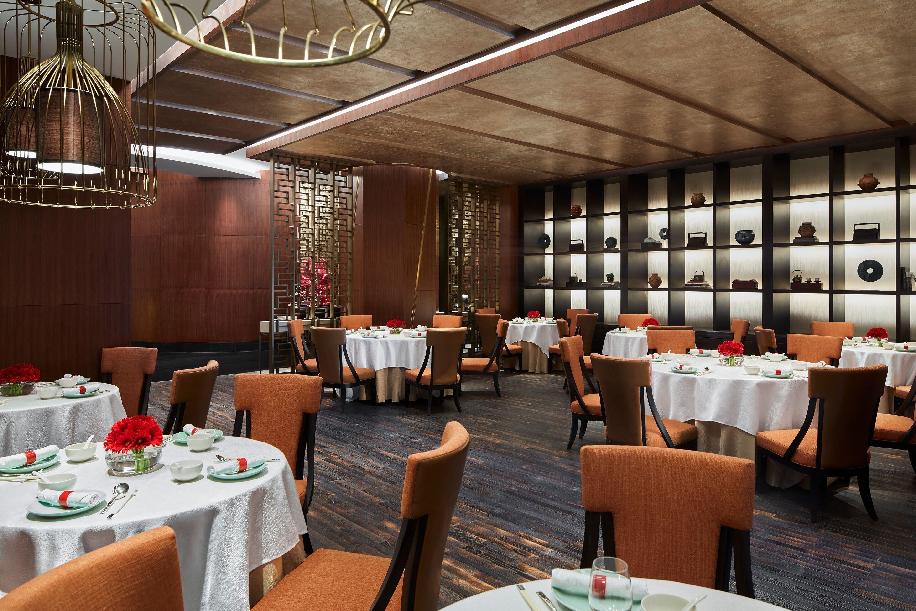 A restaurant with round tables, orange chairs, and a wall of decorative items.