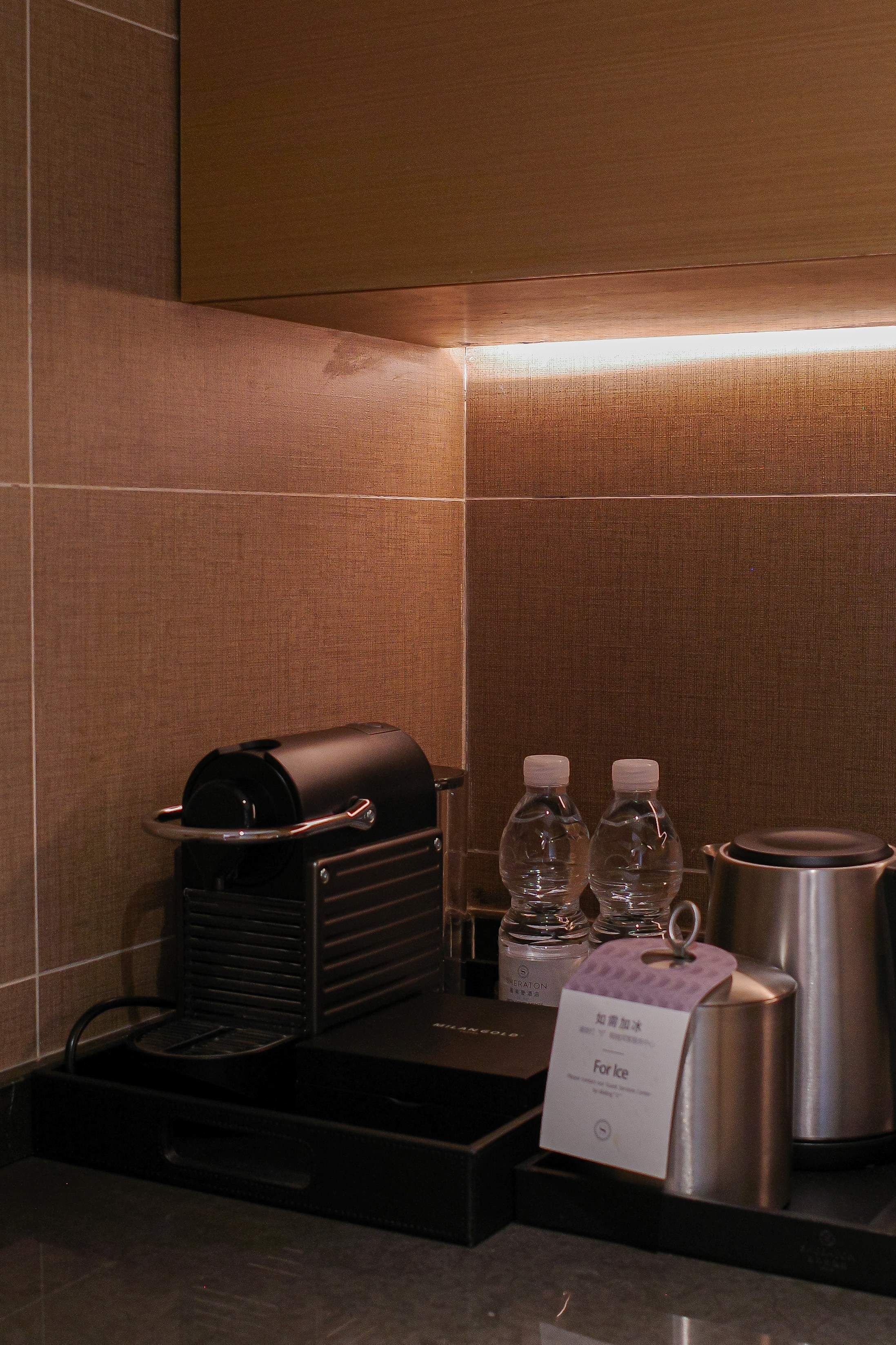 A hotel minibar with a coffee machine, two bottles of water, and a stainless steel pot.