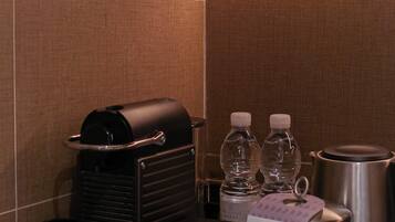 A hotel minibar with a coffee machine, two bottles of water, and a stainless steel pot.