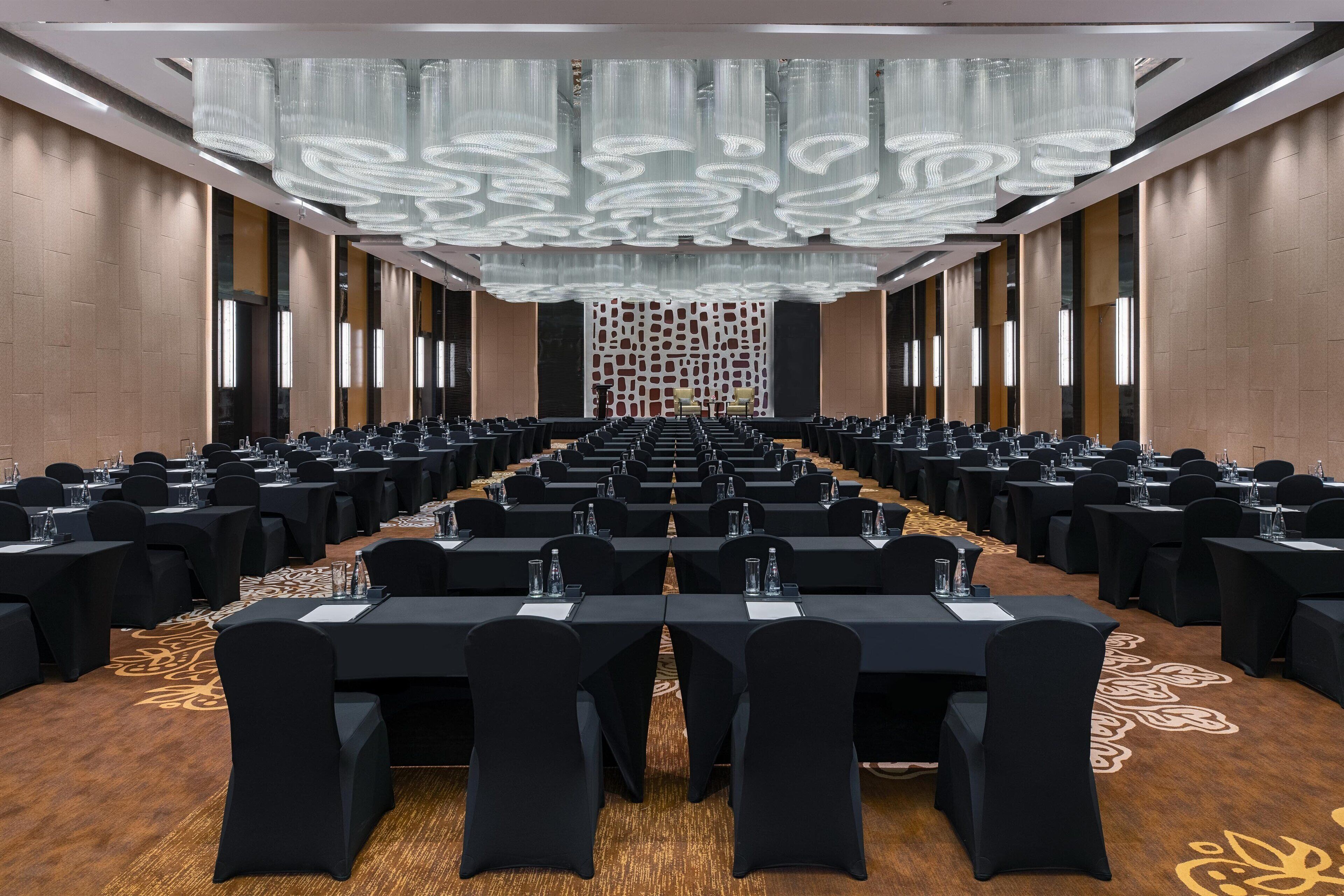 A conference room with rows of tables and chairs, a patterned carpet, and a decorative ceiling.