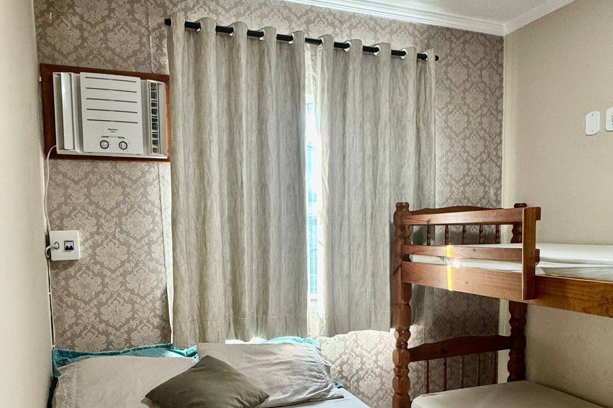 Una habitación con una cama litera, una cama individual, un calentador de pared y una ventana con cortinas.