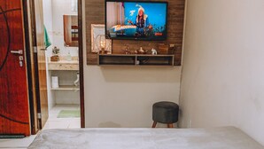 Ein Schlafzimmer mit einem Bett, einem an der Wand montierten Fernseher, einem Holzboden darunter und einer Tür zu einem anderen Raum.