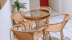 Ein Zimmer mit einem runden Glastisch, umgeben von Korbstühlen, einer roten Tür und einem grünen Fenster.