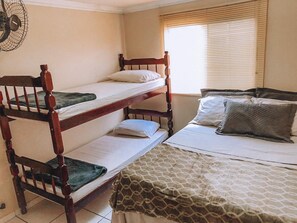 A room with bunk beds, a fan, and a window with blinds. - Acquamarine Suítes (Arraial do Cabo)