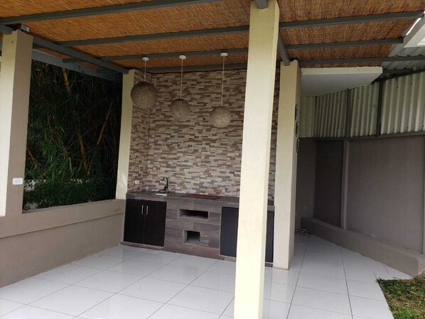 An outdoor kitchen area with a stone backsplash, built-in cabinets, and hanging spherical lights.