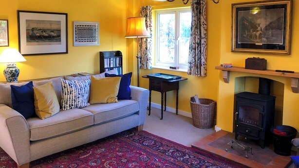 A cozy living room with a sofa, a patterned rug, a fireplace, and a bookshelf. - 4 bedroom accommodation in Hempstead, near Holt (Hempstead, near Holt)