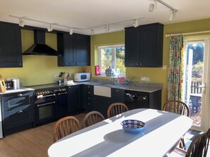 A compact kitchen with black cabinets, a microwave, a stove, and a dishwasher. There is a dining table with chairs and a bowl on it. - 4 bedroom accommodation in Hempstead, near Holt (Hempstead, near Holt)