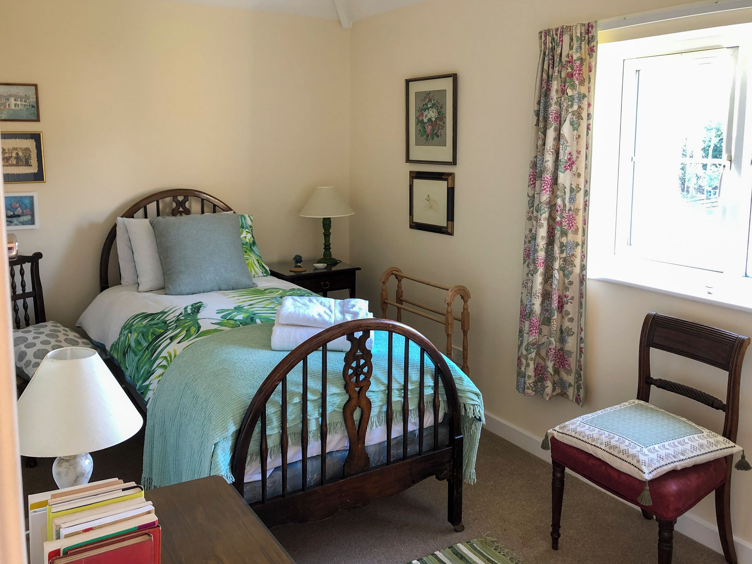 A bedroom with a bed, a chair, a nightstand, a lamp, and a window with curtains.