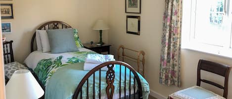 A bedroom with a bed, a chair, a nightstand, a lamp, and a window with curtains.