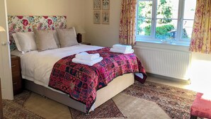 A bedroom with a bed, pillows, a nightstand, a window with curtains, and a radiator. - 4 bedroom accommodation in Hempstead, near Holt (Hempstead, near Holt)