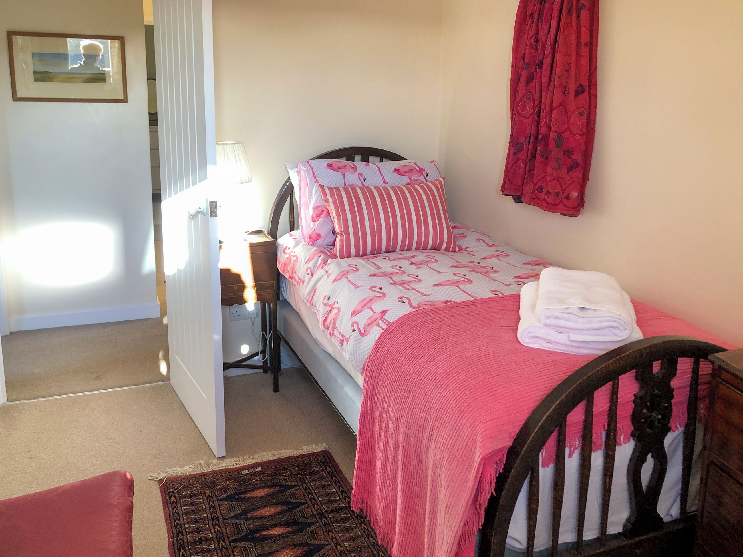 A small bedroom with a single bed, a bedside table, a lamp, a red curtain, and a framed picture on the wall.