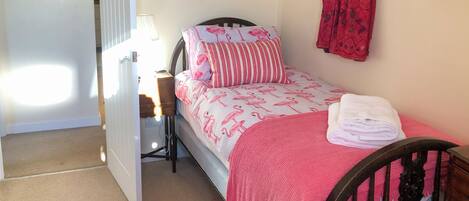 A small bedroom with a single bed, a bedside table, a lamp, a red curtain, and a framed picture on the wall.