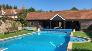 A rectangular swimming pool with a tiled deck, surrounded by a well-maintained lawn and a brick building with a tiled roof. - 4 bedroom accommodation in Hempstead, near Holt (Hempstead, near Holt)