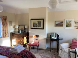 A bedroom with a bed, a dresser, a chair, a table with books, and a wall with framed pictures. - 4 bedroom accommodation in Hempstead, near Holt (Hempstead, near Holt)