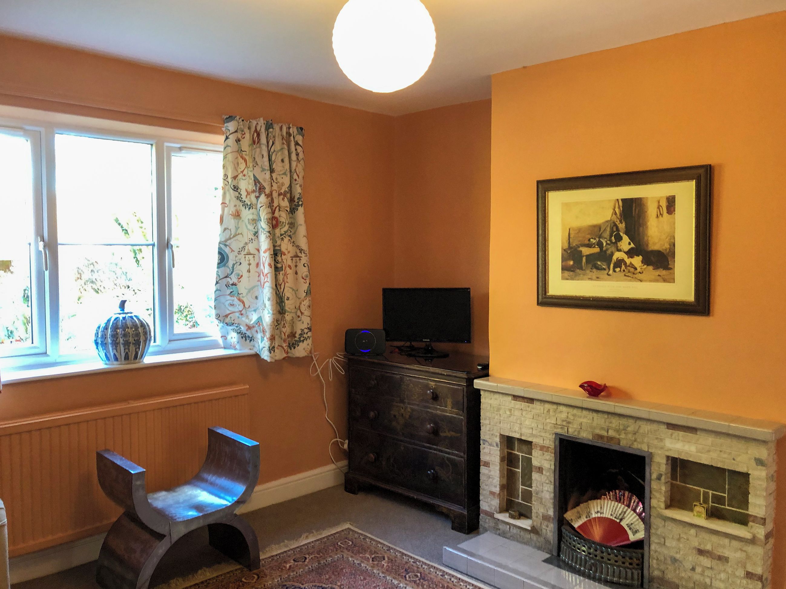 A room with a fireplace, a television, a chair, and a window with curtains.