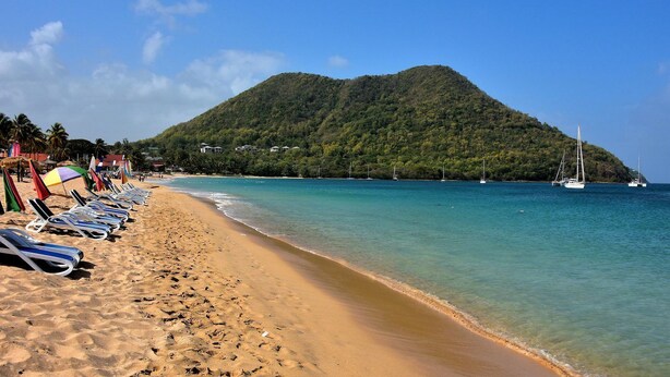A beach with lounge chairs and umbrellas, a clear blue sea, and a mountain in the background. - Careffe Suites Studio 4 - 5 mins to from Rodney Bay Village (Monchy)