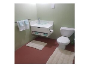 Une salle de bain avec un lavabo blanc, des toilettes et deux tapis blancs sur le sol.