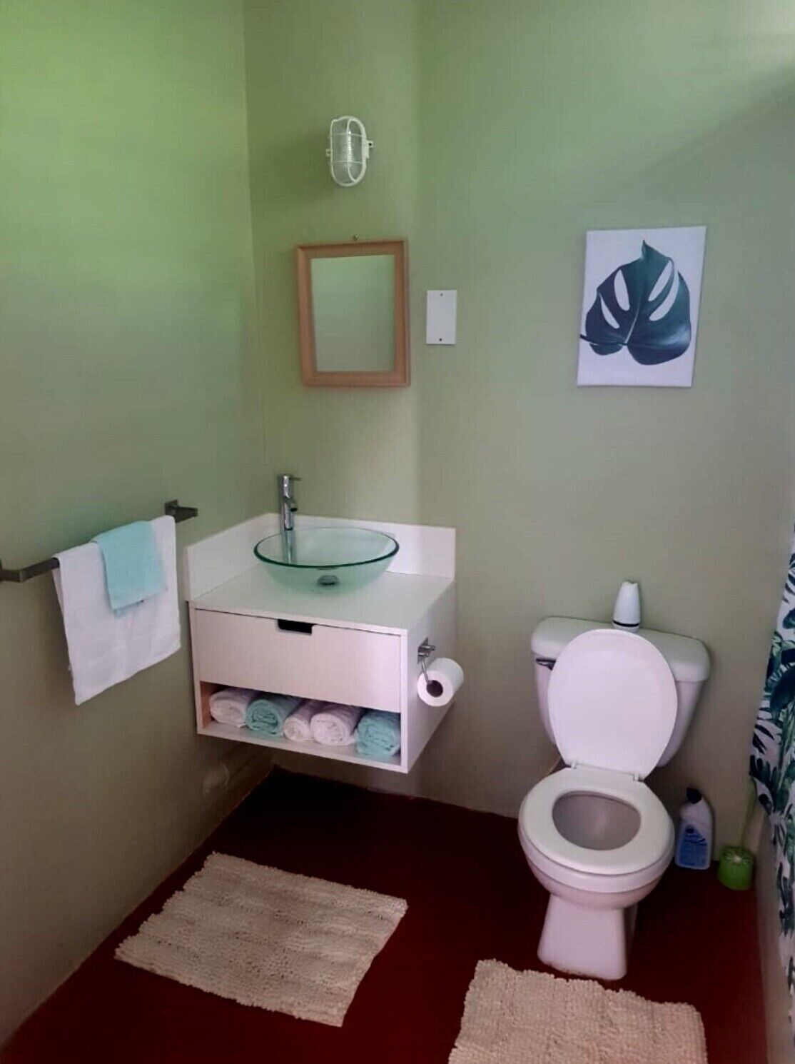 Une salle de bain avec un lavabo en verre, des toilettes blanches et un miroir.