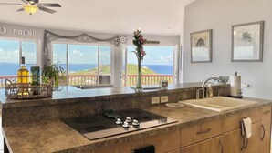 A kitchen with a large island, a view of the ocean, and a ceiling fan. - Breathtaking Panoramic Views Of The Caribbean Sea From This Luxury Villa (St. Thomas)