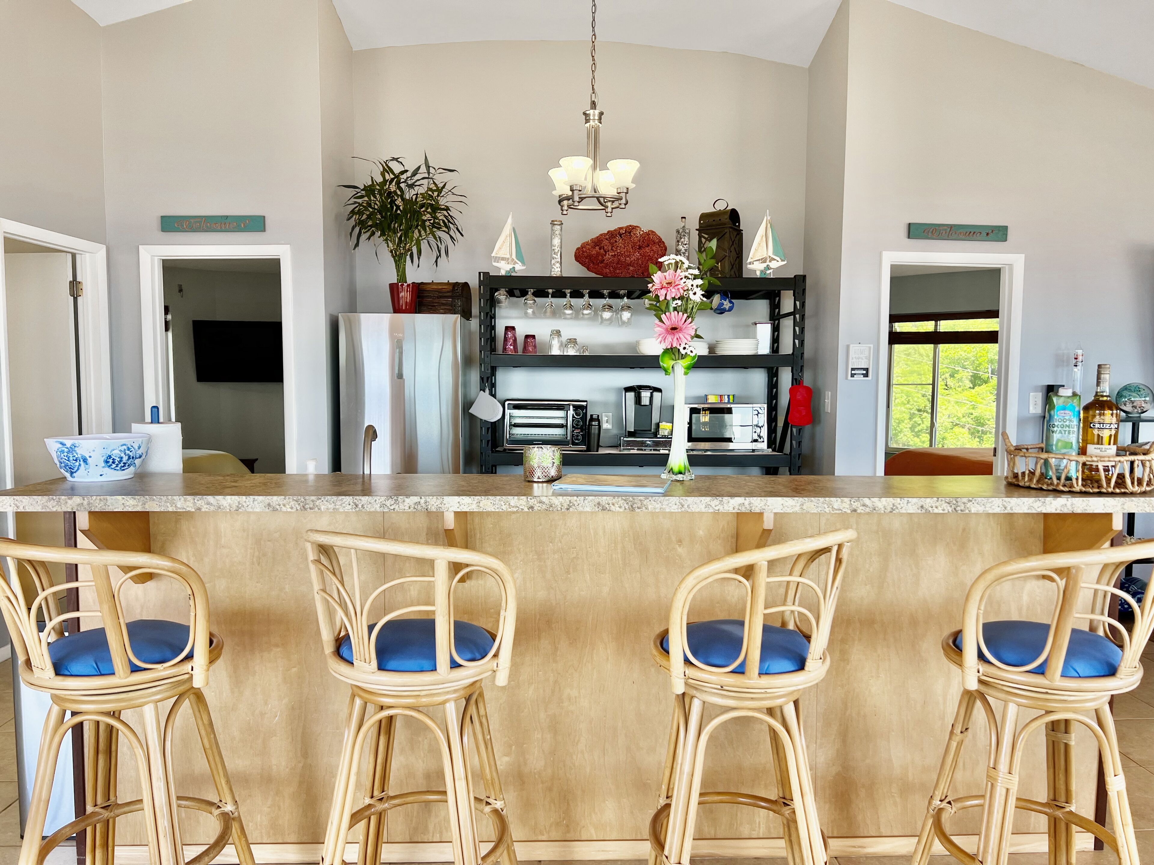 A kitchen with a central island, bar stools, a refrigerator, a coffee machine, and a potted plant.
