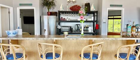 A kitchen with a central island, bar stools, a refrigerator, a coffee machine, and a potted plant.