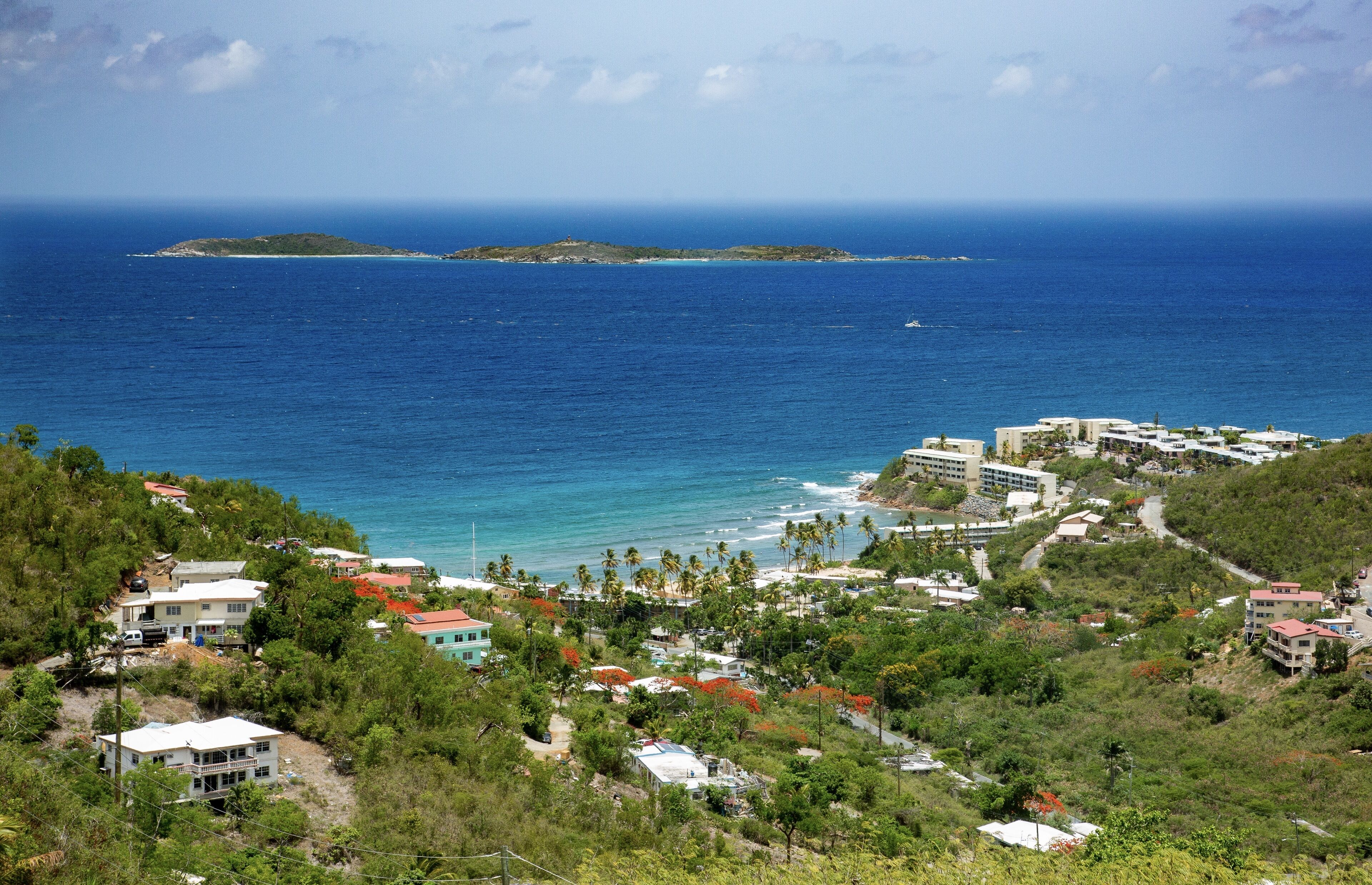 Une ville côtière avec des bâtiments qui bordent le littoral, une petite île visible au loin et une vue dégagée sur l’océan.
