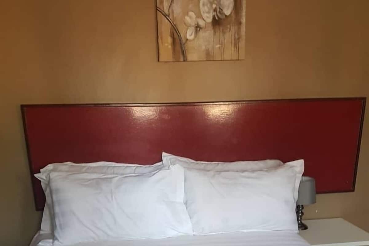 Ein Hotelzimmer mit Bett, weißer Bettwäsche, einem roten Kopfteil und einem Wandbild.