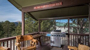 Un espacio al aire libre techado con una parrilla y bancos de madera, con vistas a un paisaje boscoso.