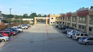 A parking lot with multiple rows of parked cars, a building with a flat roof, and a clear sky. - Crystal Inn Downtown (Houston)