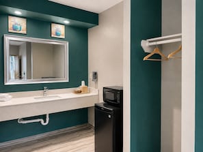A modern bathroom with a teal accent wall, a large mirror, a sink with a towel rack, a black microwave, and a wooden towel holder. - Crystal Inn Downtown (Houston)