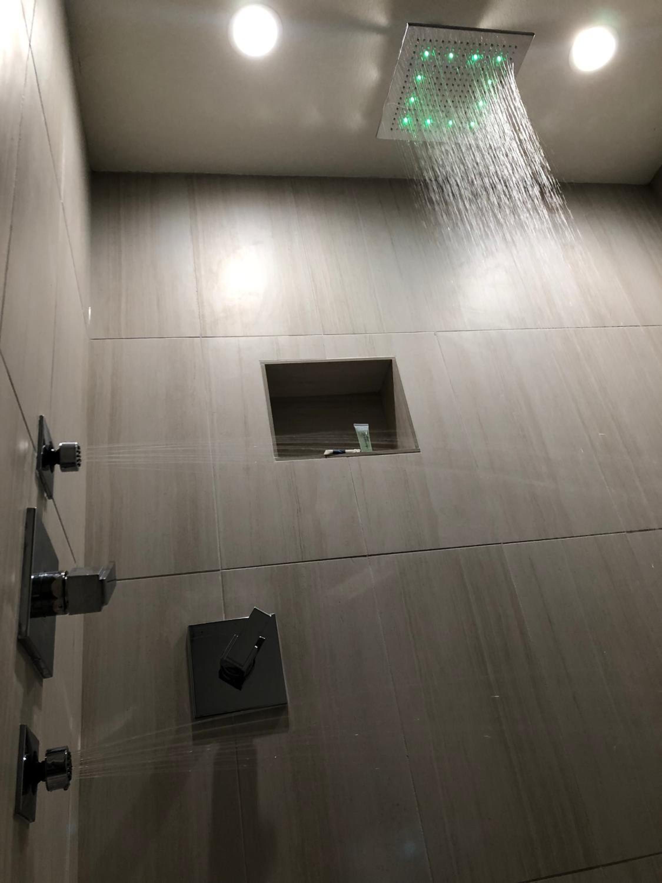 A modern shower with a square window, a control panel, and a ceiling-mounted showerhead.