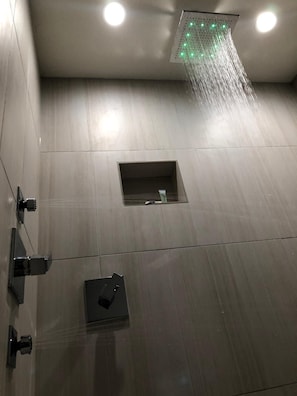 A modern shower with a square window, a control panel, and a ceiling-mounted showerhead. - Crystal Inn Downtown (Houston)