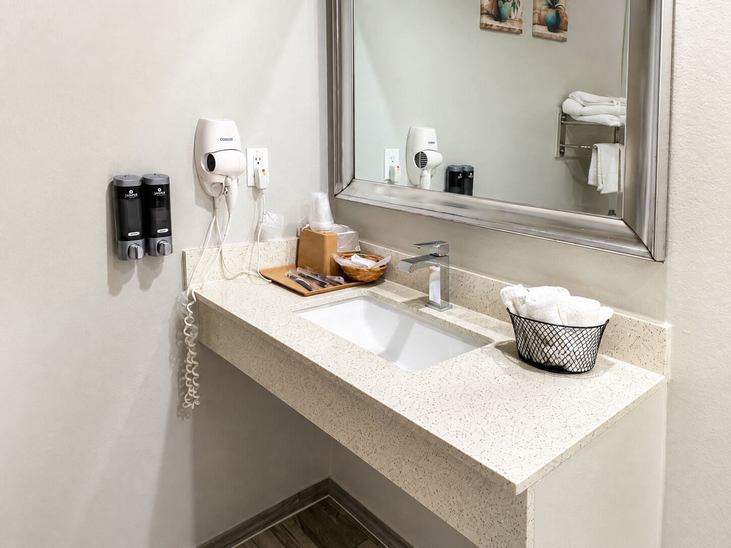 Un baño de hotel con un lavamanos, un espejo, un secador de pelo y un perchero para toallas.