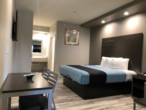 Ein Hotelzimmer mit Bett, Schreibtisch, Stuhl, Nachttisch und einem an der Wand befestigten Fernseher.