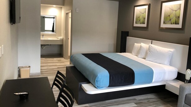 A modern hotel room with a bed, a desk, and a chair. There is a bathroom visible in the background. - Crystal Inn Downtown (Houston)