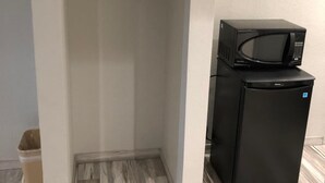 A compact kitchen with a black refrigerator and microwave, a wooden hanger on a white shelf, and a grey and white patterned floor. - Crystal Inn Downtown (Houston)