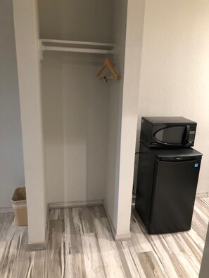 Ett kompakt kök med ett svart kylskåp och en mikrovågsugn, en trägalge på en vit hylla och ett grått och vitt mönstrat golv.
