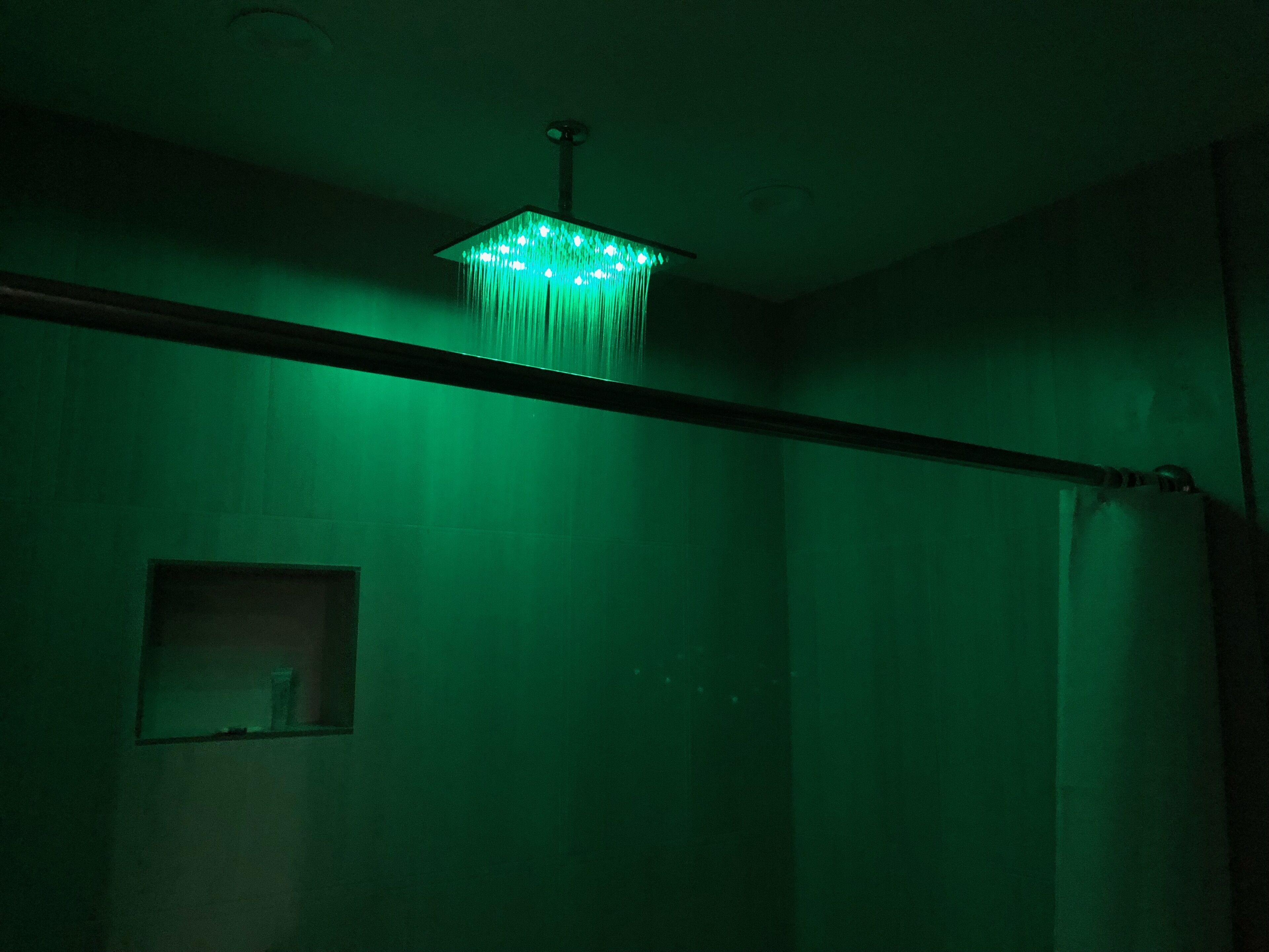 A room with a green-lit chandelier, a visible window, and a curtain rod.