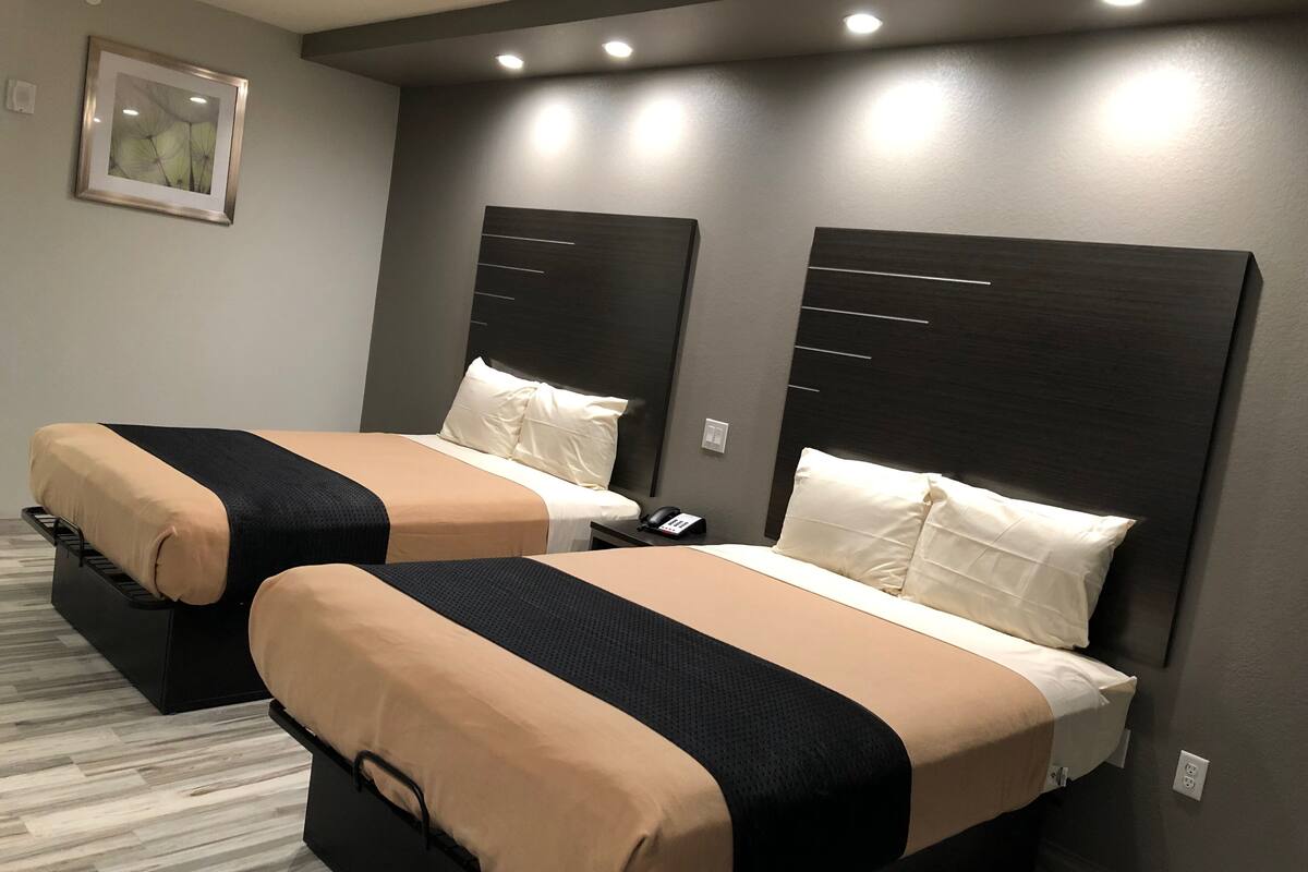 Duas camas lado a lado, com cabeceiras, um quadro na parede e um telefone na mesinha de cabeceira.