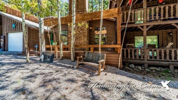 A rustic cabin with a wooden deck, a bench, and a stone wall. - Timbers Lodge | Your Ruidoso Retreat w/ Hot Tub Bliss, Wildlife Views & Cozy Comforts (Ruidoso)